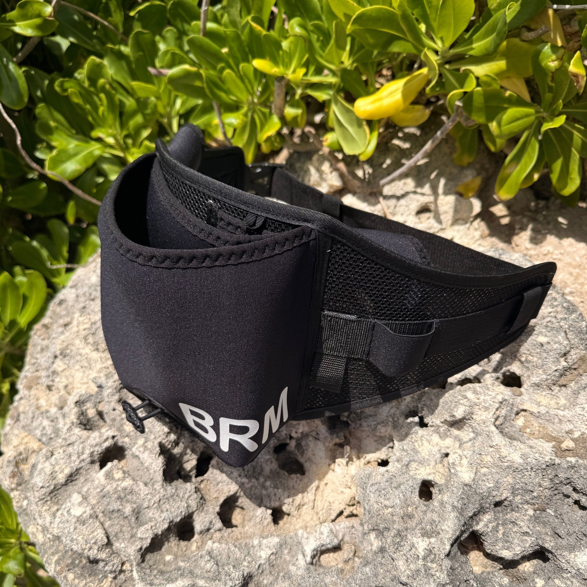 Black parawing stash belt with 'BRM' branding on a rock with greenery in the background