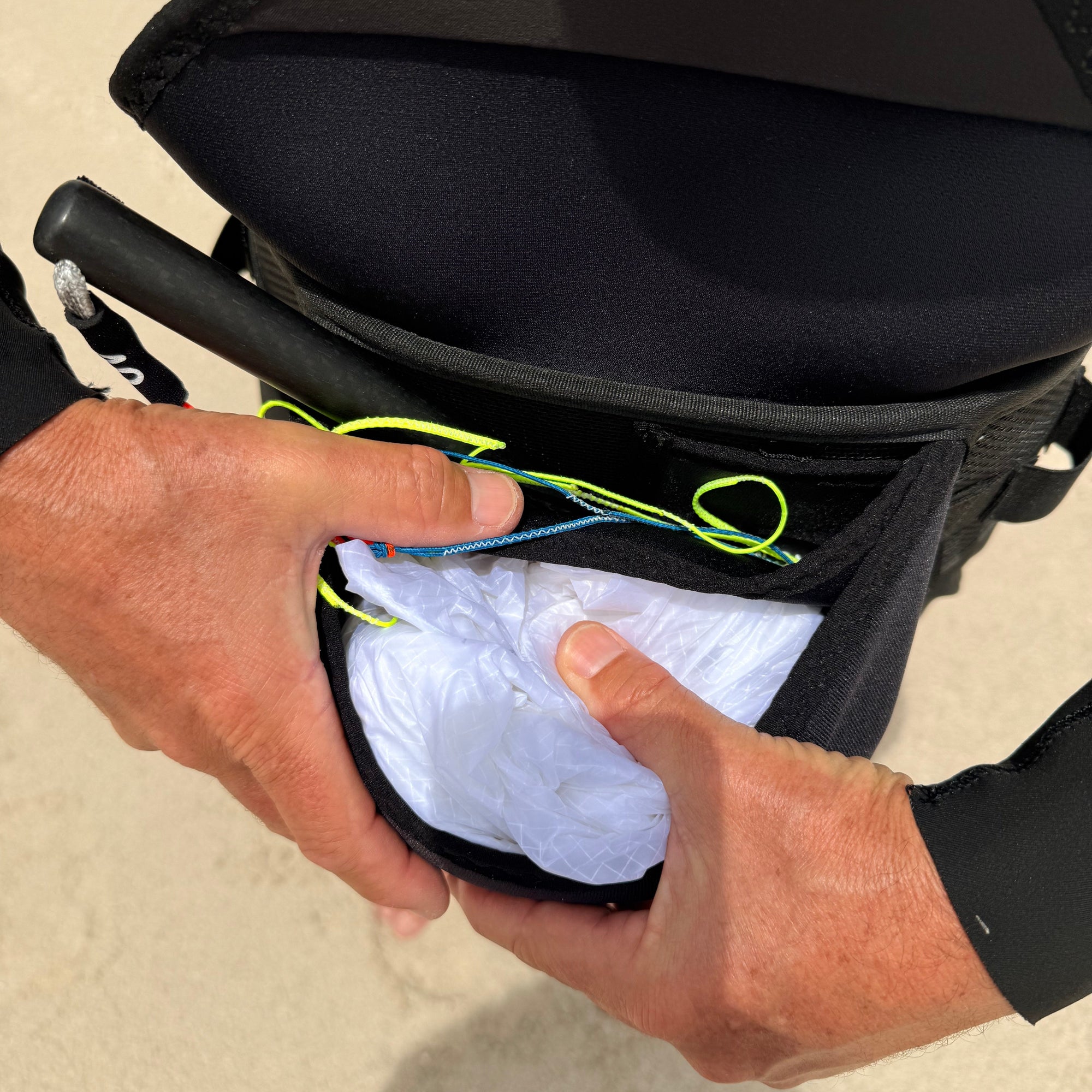 Person placing  a white parawing inside a black bag on a sandy background
