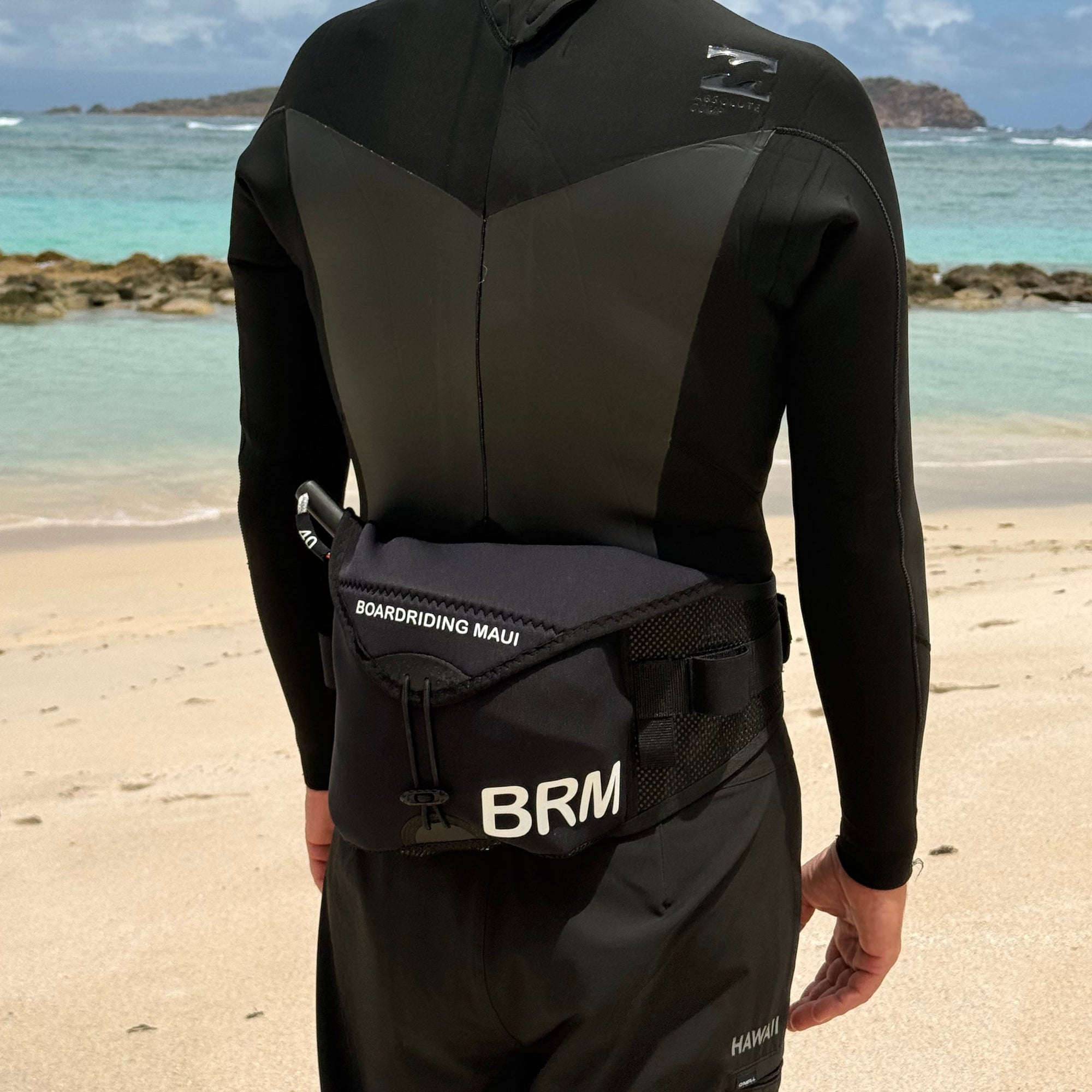 Person wearing a black wetsuit and parawing belt on a beach