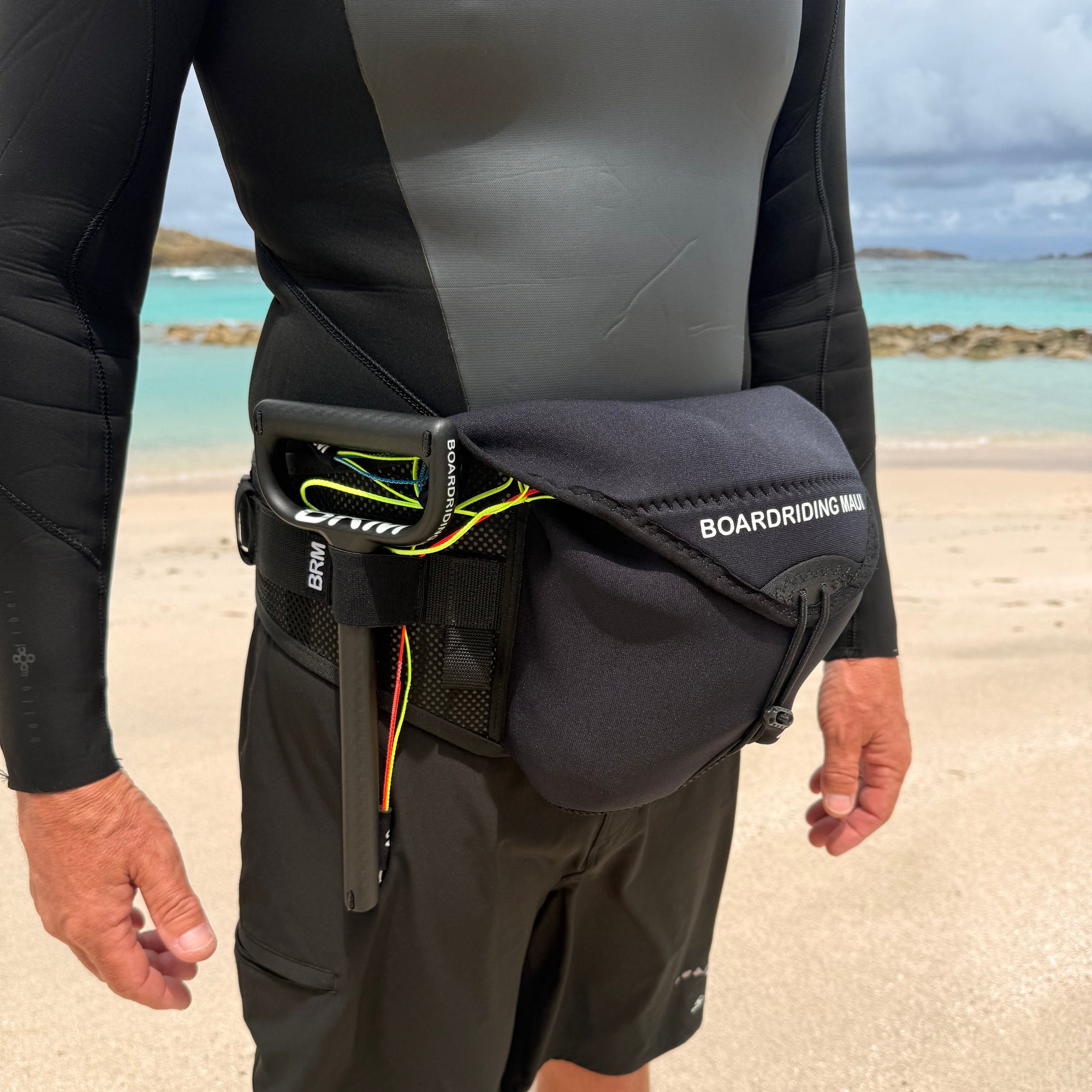 Person wearing a wetsuit and boardshorts with a waist bag on a beach.